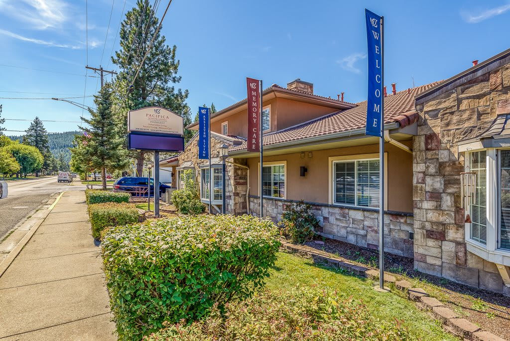A restaurant building with banners and hedges lining the sidewalk.