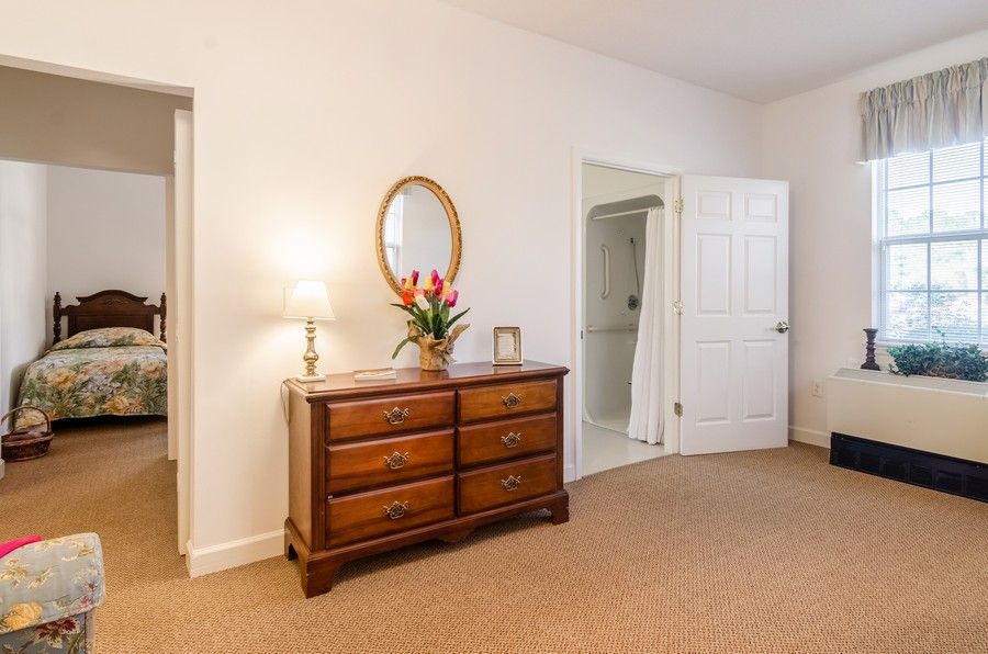 A cozy bedroom with a wooden dresser, an oval mirror, and a decorative lamp.