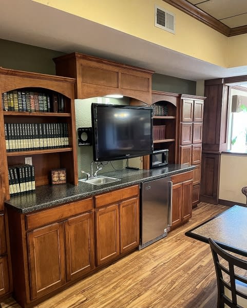 A cozy office space featuring wooden cabinets, a television, and bookshelves filled with books.