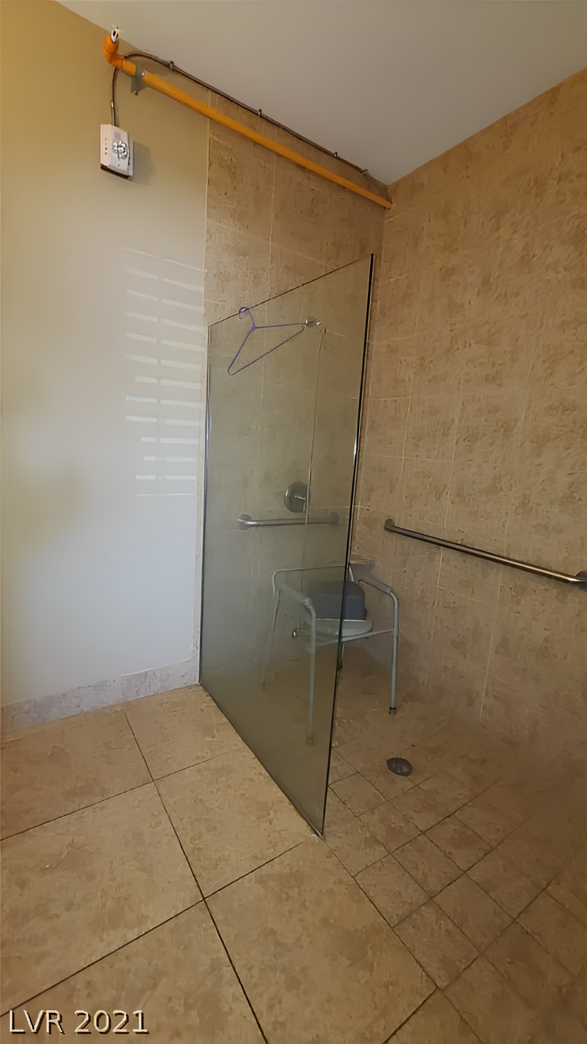 A spacious bathroom with a glass-partitioned shower, featuring a handrail for accessibility.