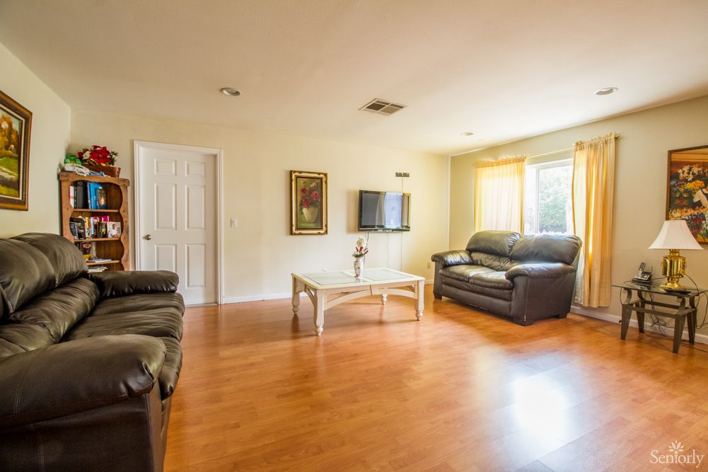 A bright and spacious living room with a wooden floor, featuring leather couches, a coffee table, and a wall-mounted television.