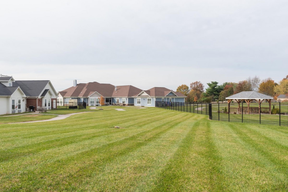 A view of suburban houses with a neatly maintained lawn and fence under a cloudy sky.