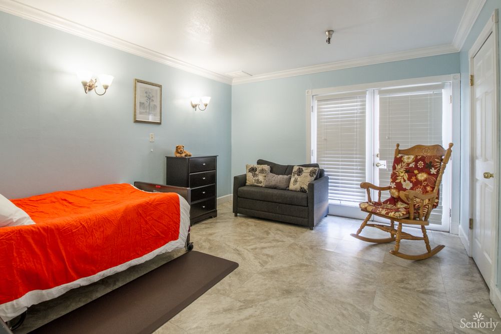 A cozy bedroom featuring a bed with an orange blanket, a sofa, and a rocking chair against blue walls.