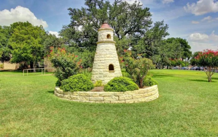 A small decorative lighthouse surrounded by greenery in a park.
