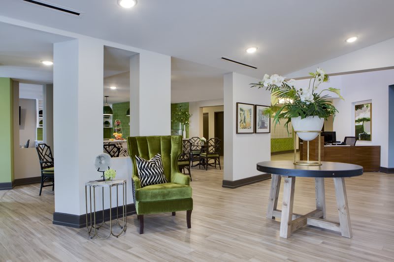 A modern lobby area featuring a green velvet chair, a round table with decorative plants, and stylish wall art.