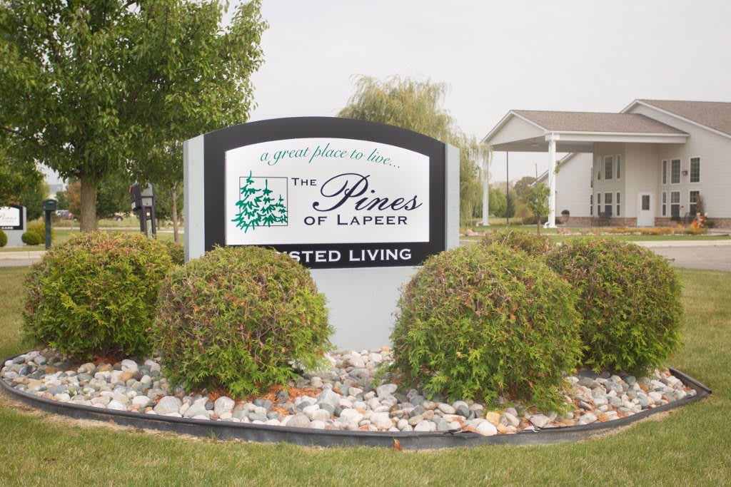 Sign for The Pines of Lapeer Assisted Living surrounded by landscaping.