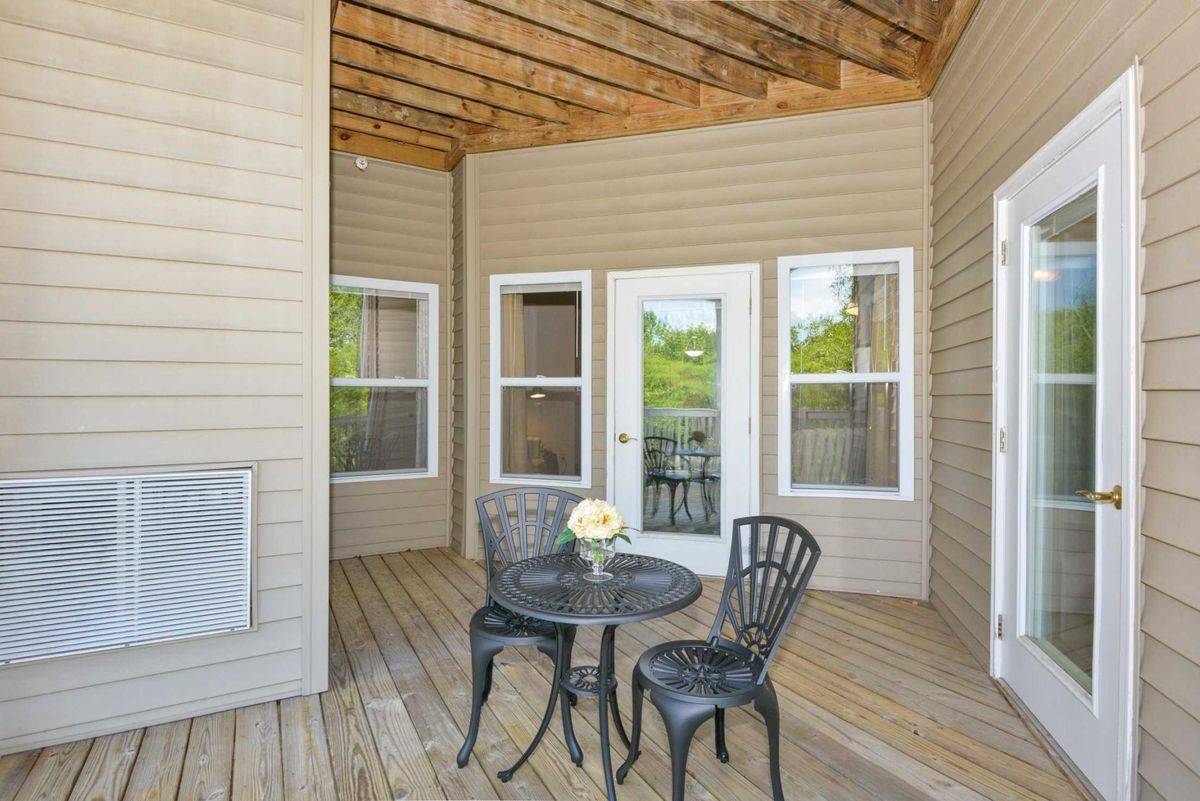 A cozy outdoor patio with a small table, two chairs, and a vase of flowers on a wooden deck.
