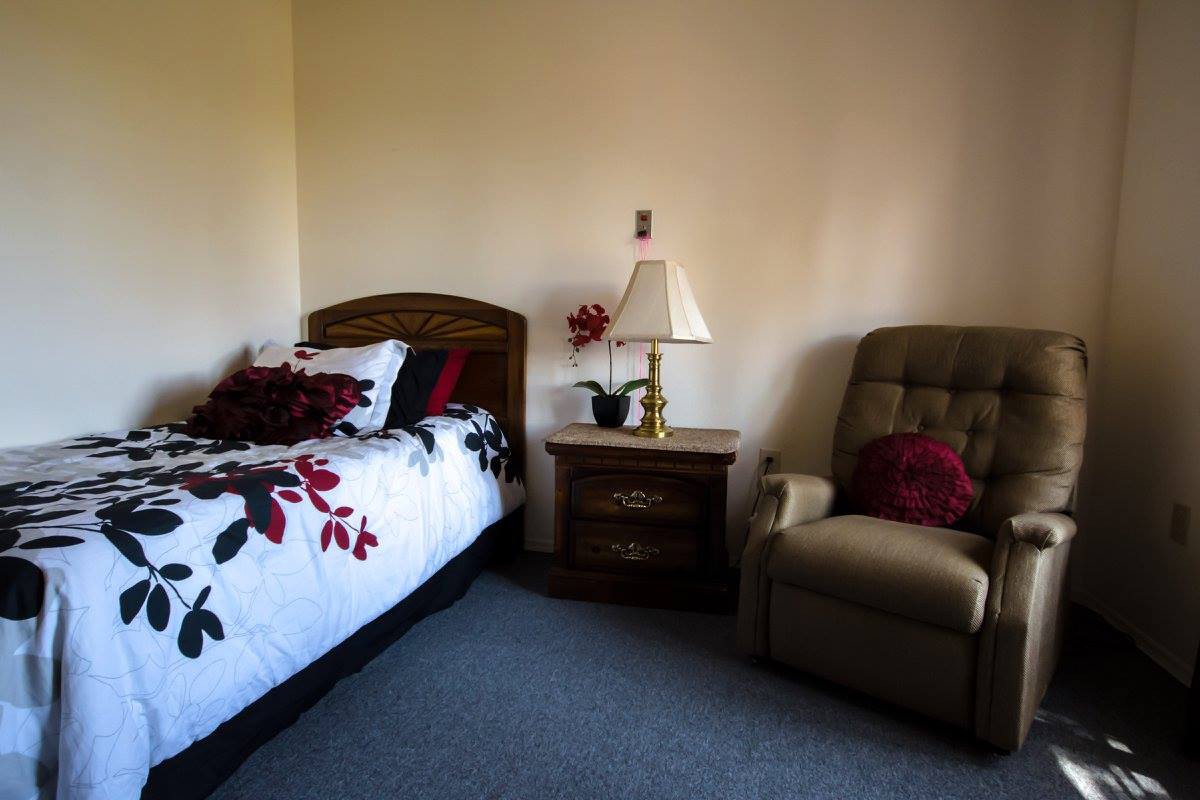 A cozy bedroom corner featuring a bed with floral bedding, an armchair, and a nightstand with a lamp.