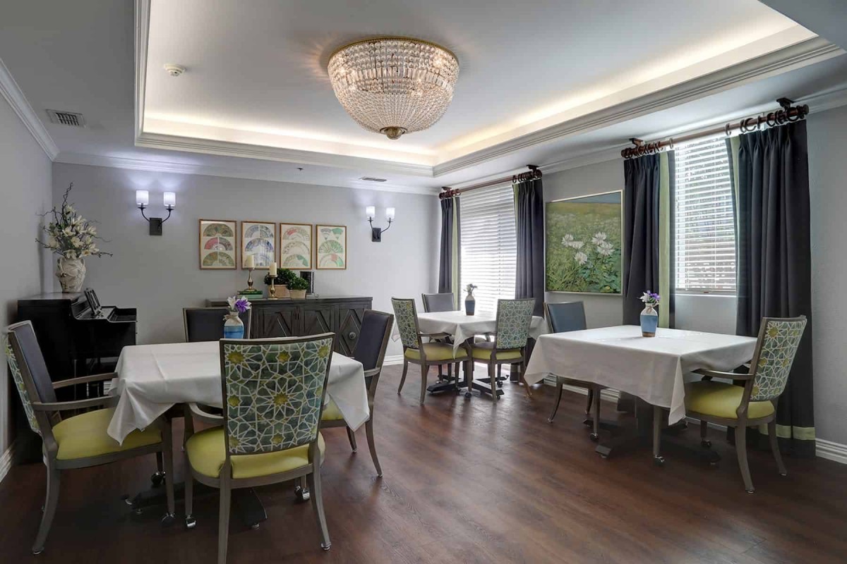 A spacious dining room with elegantly set tables, comfortable chairs, and a chandelier providing ambient lighting.