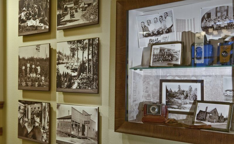 A collection of vintage black and white photographs displayed on a wall, accompanied by an antique camera in a museum setting.
