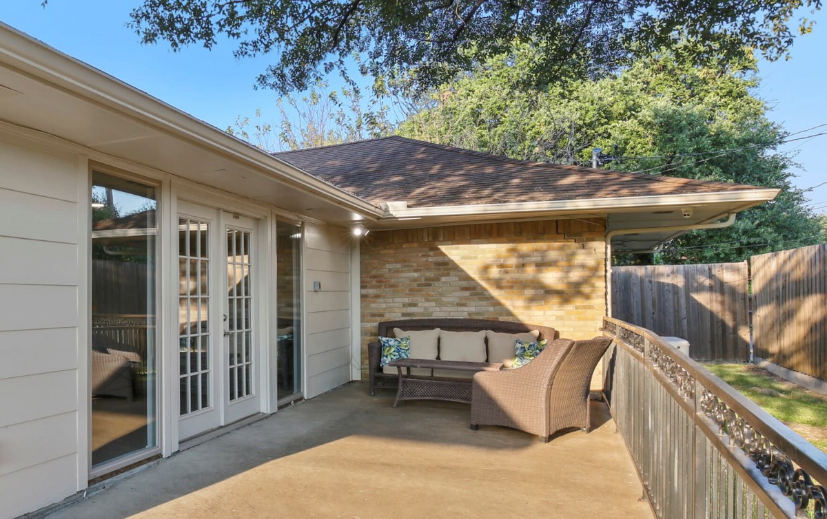 A cozy patio area with outdoor seating, located outside a house with French doors and surrounded by lush trees.