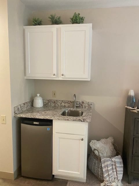 A compact kitchen area with a sink, countertop, cabinets, and a small refrigerator.