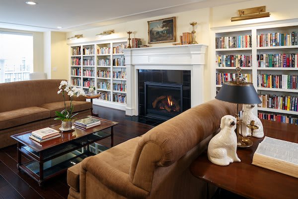 A cozy living room with a fireplace, surrounded by bookshelves and comfortable seating.