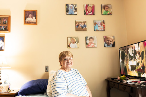 An elderly woman sitting in her room, surrounded by cherished family photos displayed on the wall.