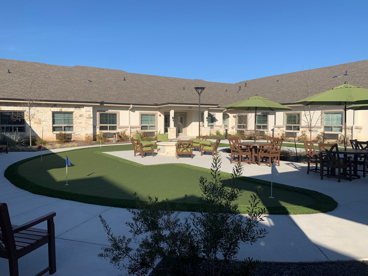 A sunny courtyard with outdoor seating and a well-maintained lawn surrounded by a building.