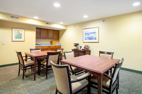 A well-lit meeting room featuring several wooden tables and upholstered chairs, with artwork on the wall.