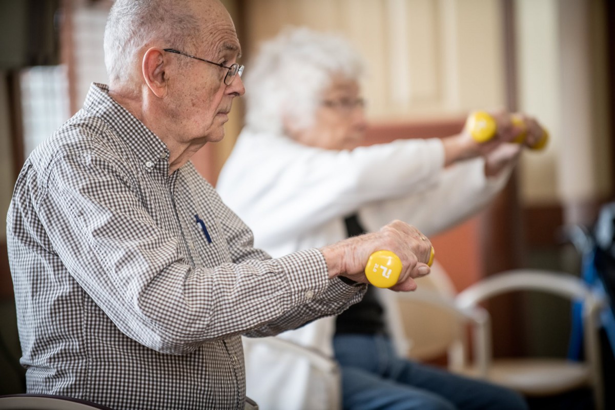 Elderly individuals participating in a seated exercise session with small weights.