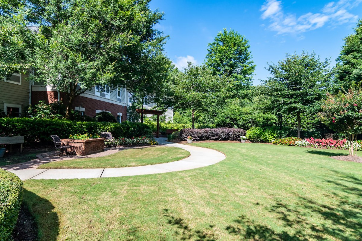 A scenic backyard garden featuring a lush lawn, curved pathway, and surrounding trees.