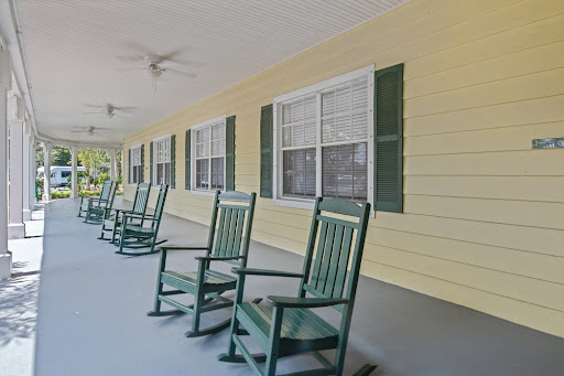 A peaceful porch with green rocking chairs against a yellow wall, perfect for relaxation.