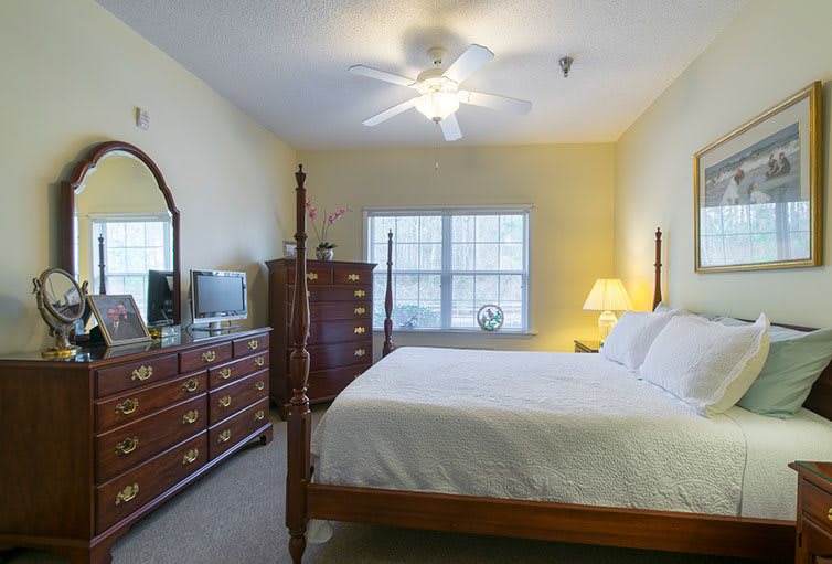 A cozy bedroom with classic wooden furniture, featuring a bed, dresser, mirror, and a well-lit lamp by the window.