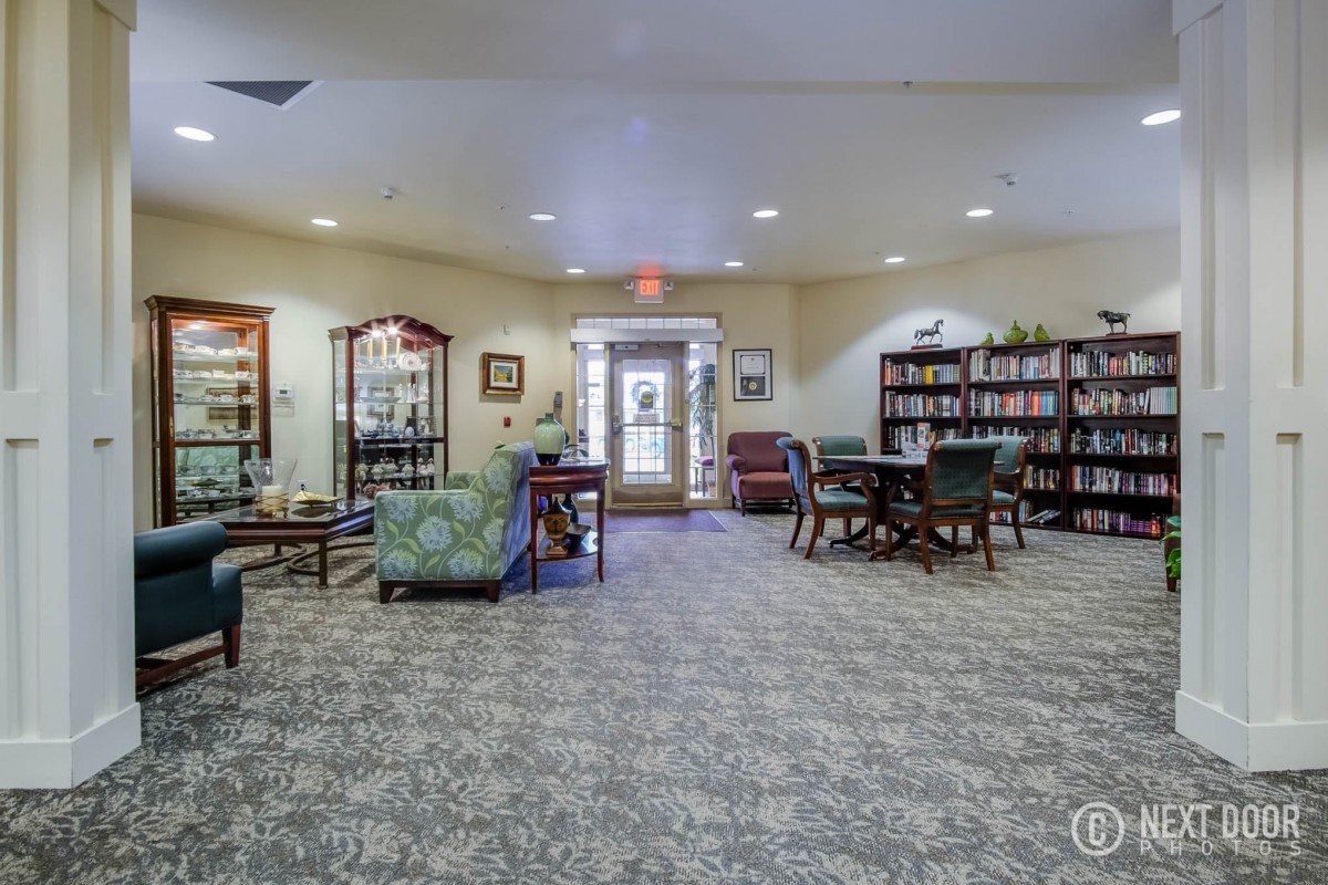 A cozy library interior with bookshelves, seating areas, and a carpeted floor.