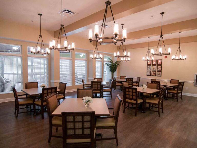 A cozy dining room with multiple tables, chairs, and elegant chandeliers.