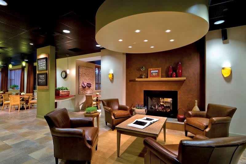 A modern and cozy living room featuring a fireplace, comfortable armchairs, a wooden table, and ambient lighting.