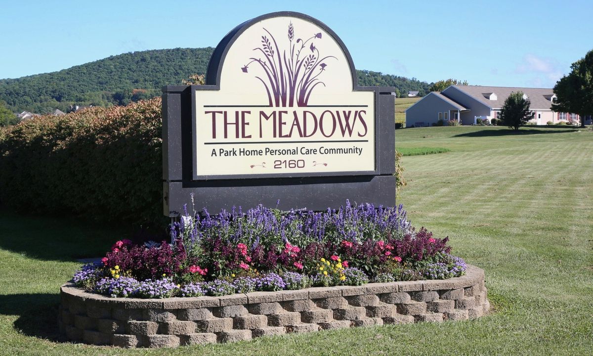 A well-maintained sign for 'The Meadows' personal care community surrounded by vibrant flowers.