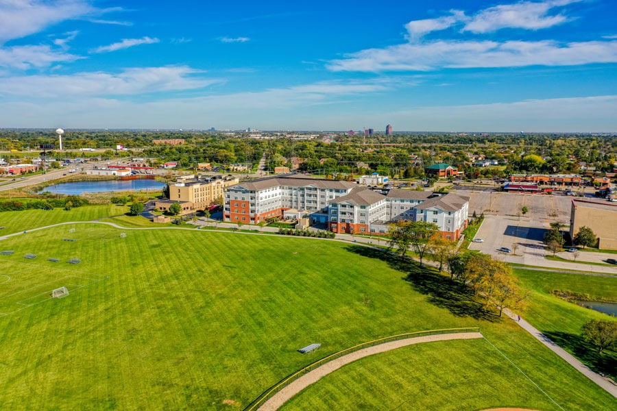 A scenic aerial view of a campus with expansive green fields and pathways, set against an urban skyline.