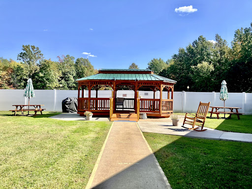 A serene outdoor space featuring a wooden gazebo surrounded by lush grass and a clear blue sky.