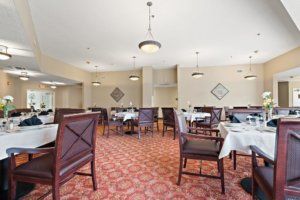 A spacious dining room with neatly arranged tables and chairs, featuring elegant light fixtures and patterned carpet.
