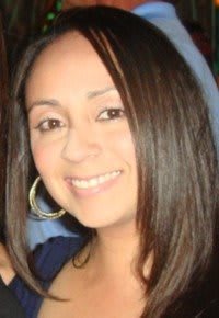 A woman smiling with long hair and hoop earrings.