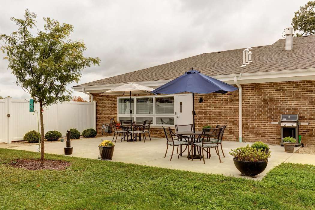 A peaceful backyard patio with tables, chairs, and a blue umbrella.