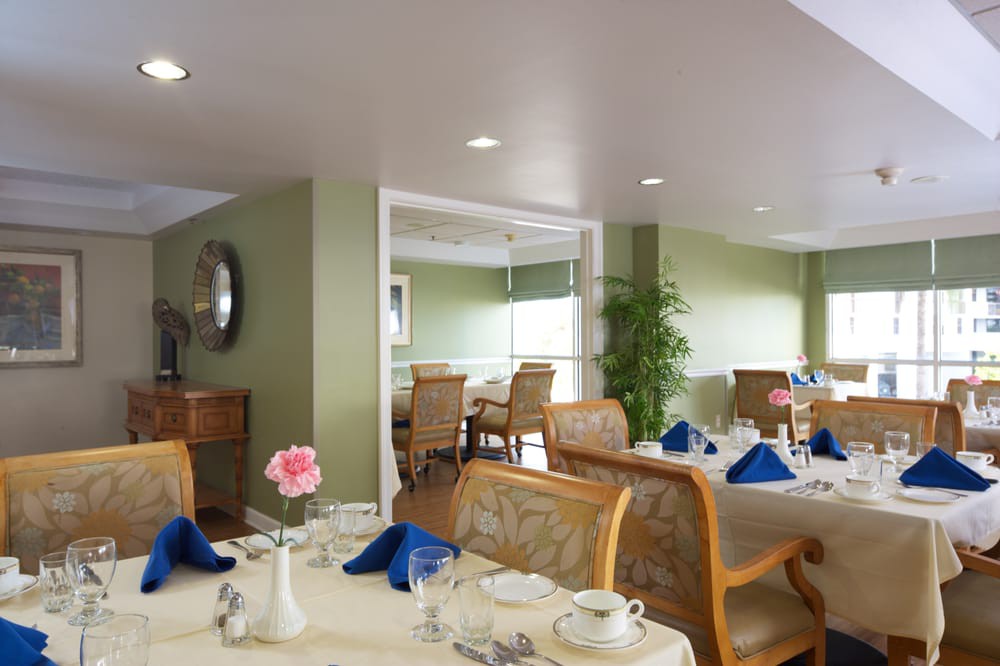 A cozy dining room with neatly arranged tables and chairs, featuring blue napkins and floral decor.