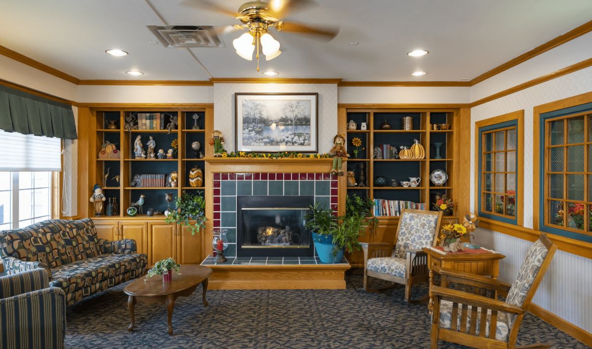 A cozy living room featuring a fireplace, surrounded by wooden bookshelves and comfortable seating.