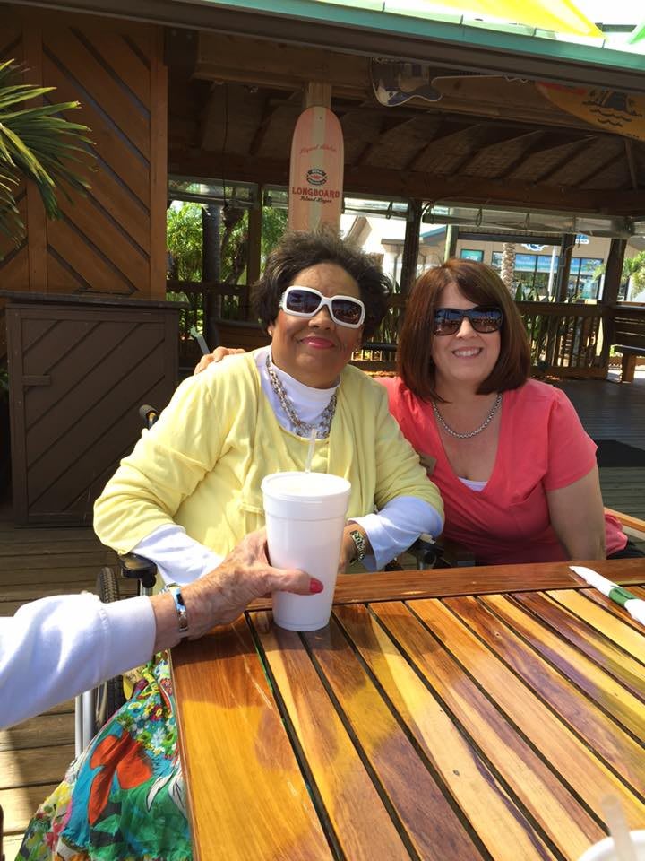 Two friends enjoying a sunny day outdoors, wearing sunglasses and sitting at a wooden table.
