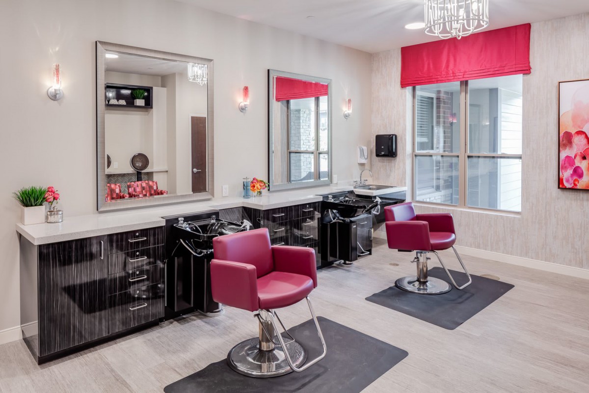 A modern hair salon interior featuring red chairs and large mirrors.