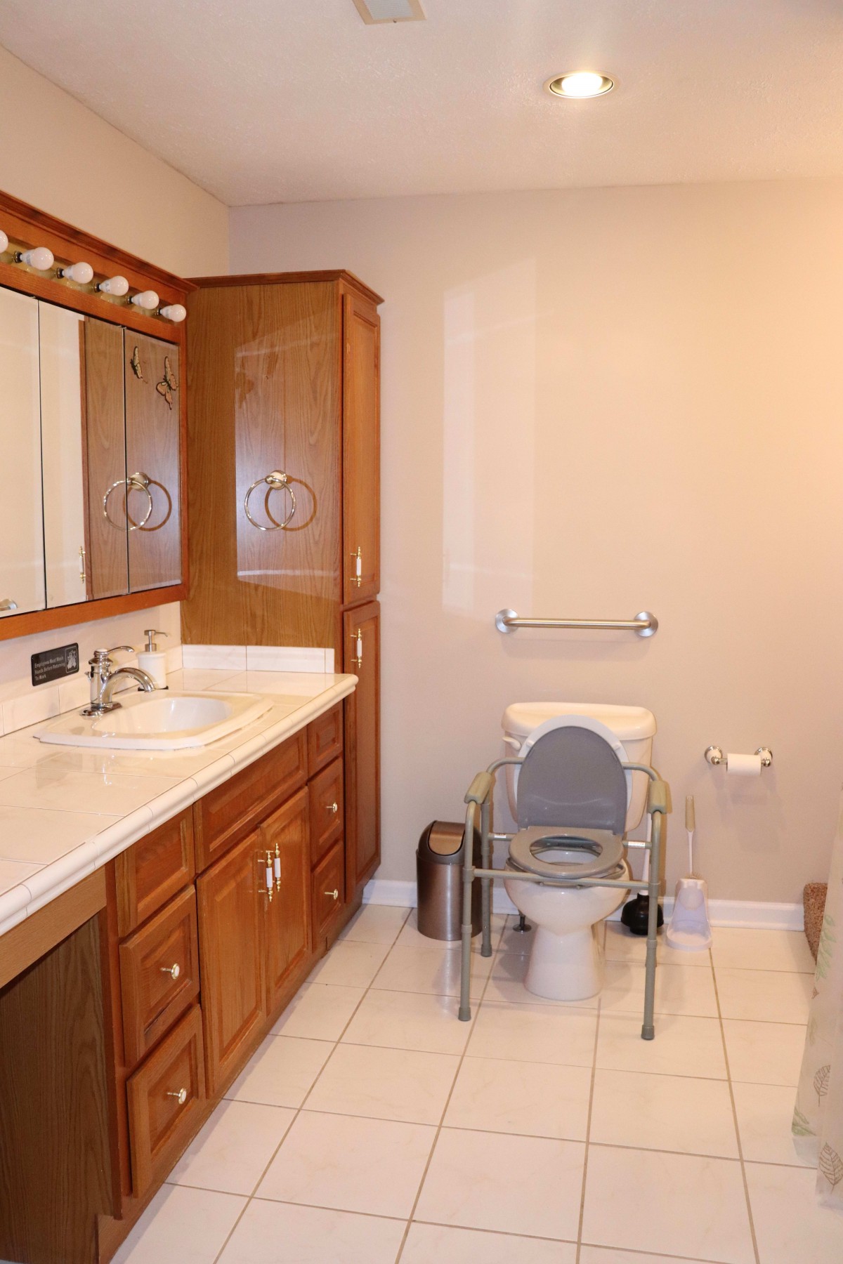 A bathroom featuring a large mirror, wooden cabinets, and a raised toilet seat with a grab bar.