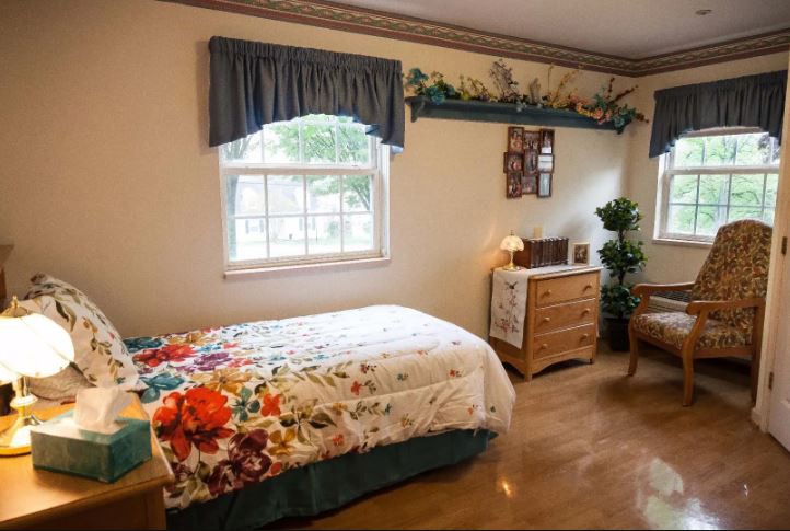 A cozy bedroom with a single bed featuring a floral bedspread, a dresser, and a potted plant by the window.