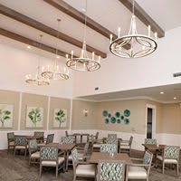 A spacious dining room with chandeliers and modern decor, featuring tables and chairs arranged neatly.