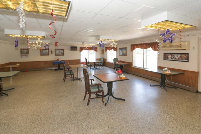 A spacious dining area with tables and chairs, adorned with ceiling decorations and well-lit by large windows.