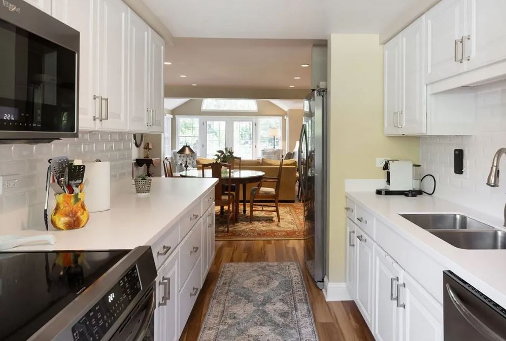 A modern kitchen with white cabinets and stainless steel appliances leading to a dining area with hardwood flooring.