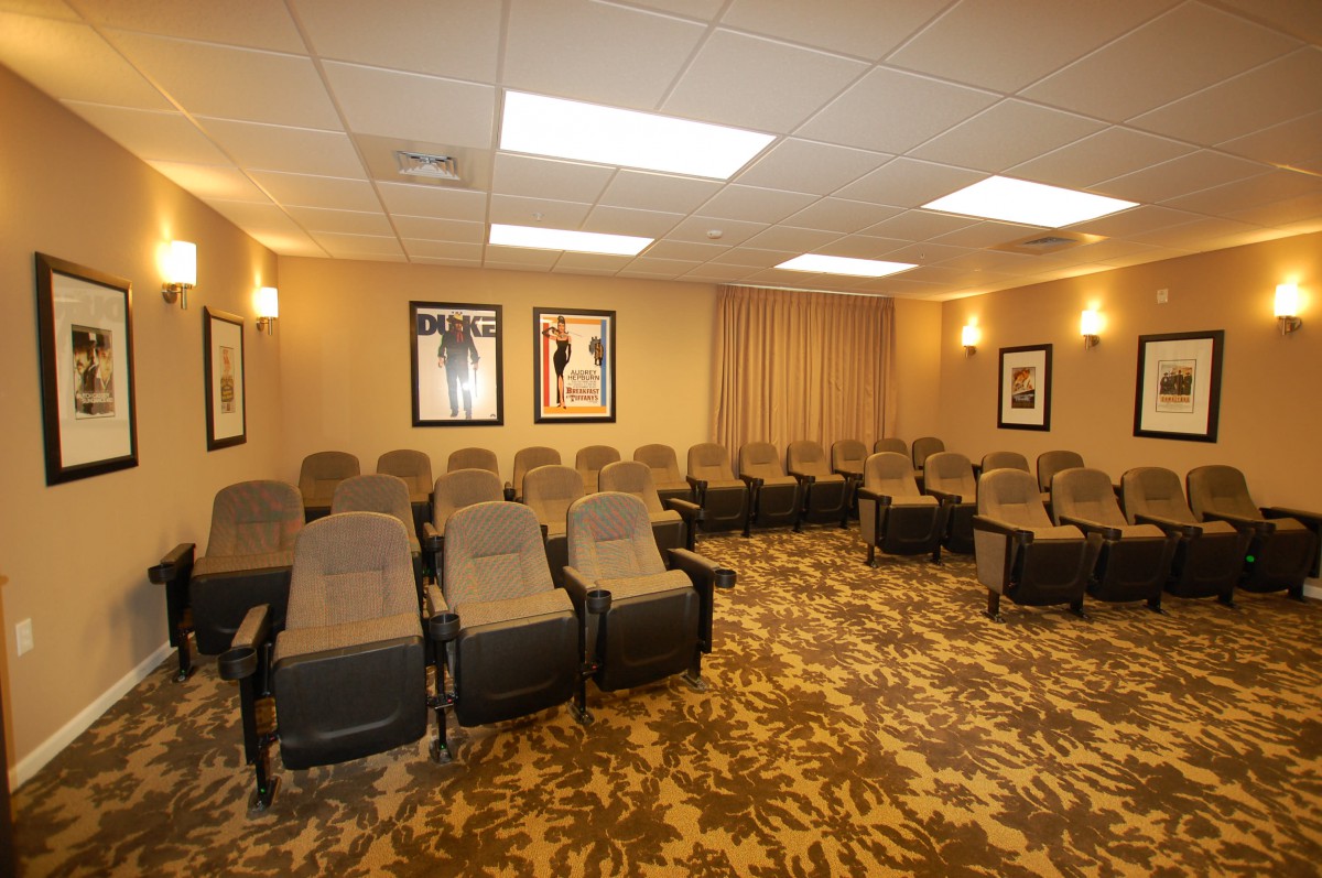 A cozy home theater room with multiple rows of plush seating and framed posters on the walls.