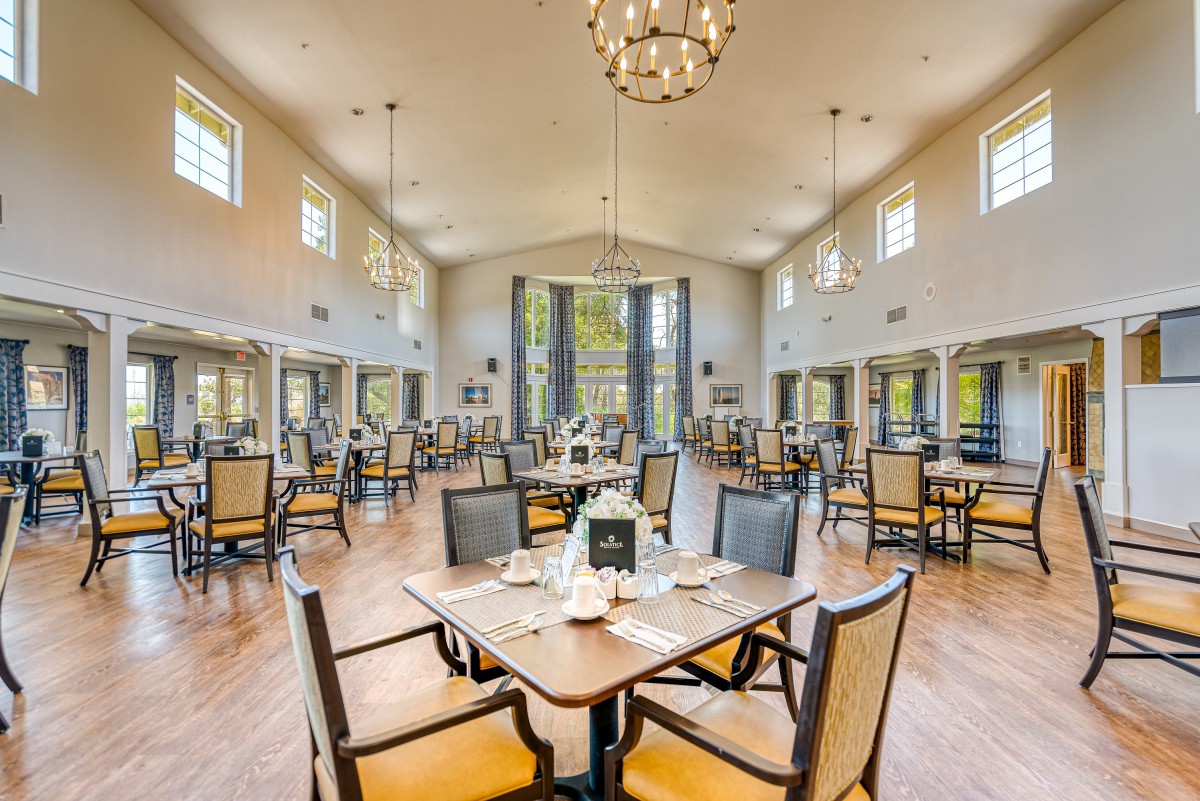 A spacious and elegantly designed dining area with neatly arranged tables and chairs, illuminated by chandeliers.