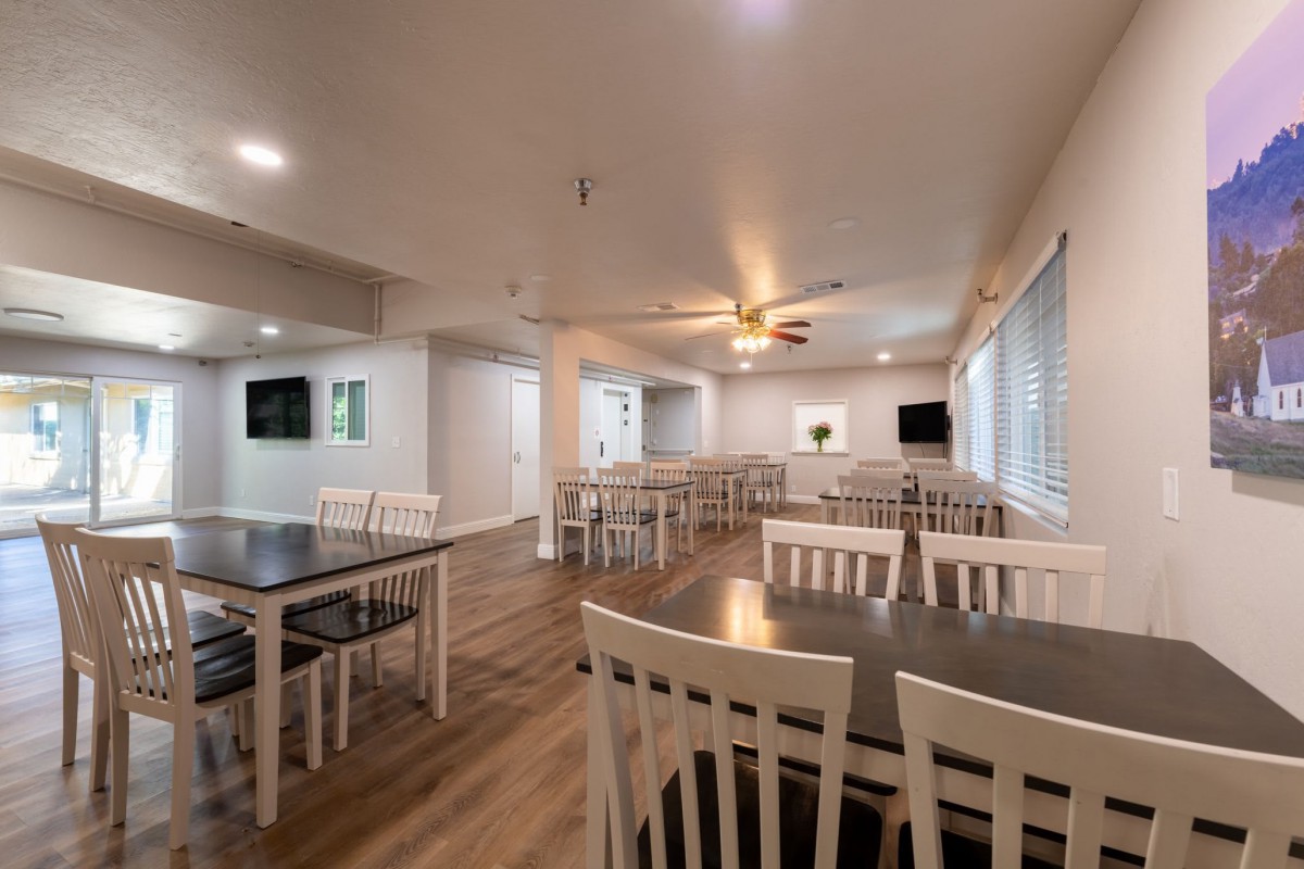 A modern dining area with multiple tables and chairs, featuring wood flooring and bright lighting.