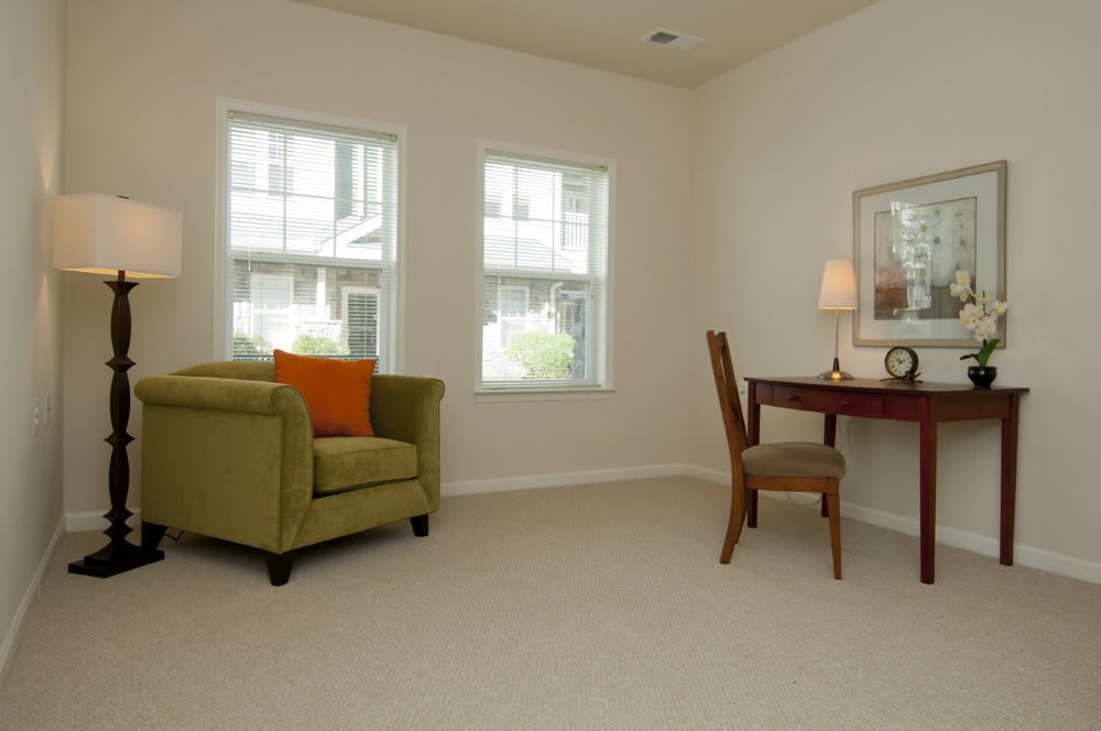 A cozy living room corner with an armchair and a desk illuminated by natural light.