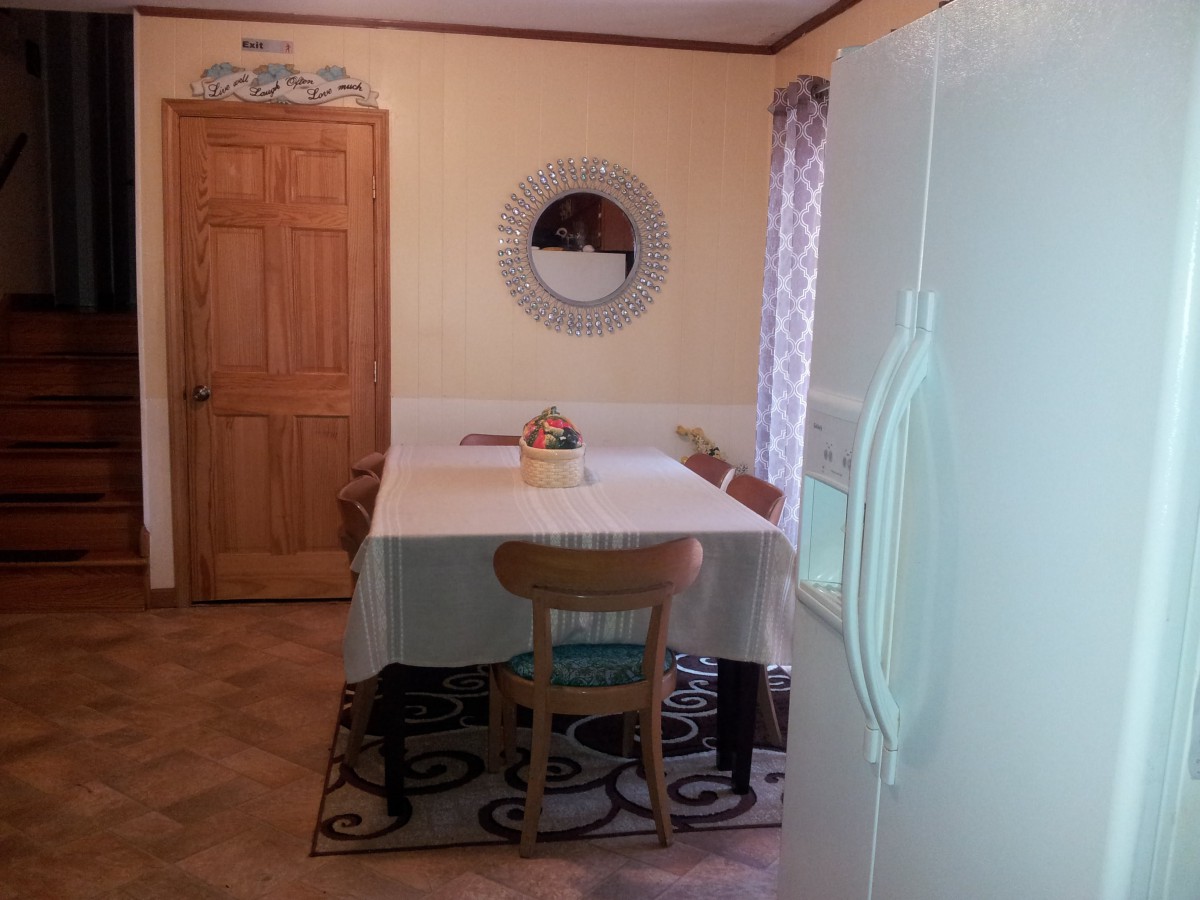 A cozy kitchen dining area with a table and chairs, featuring a mirror on the wall and a refrigerator in view.