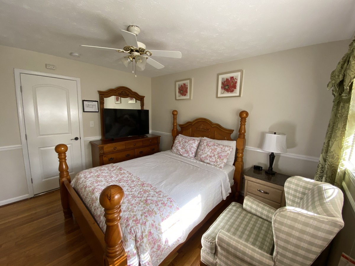 A cozy bedroom with a wooden double bed, ceiling fan, and a television on a dresser.