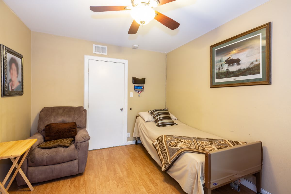 A cozy bedroom with a single bed, armchair, and ceiling fan.