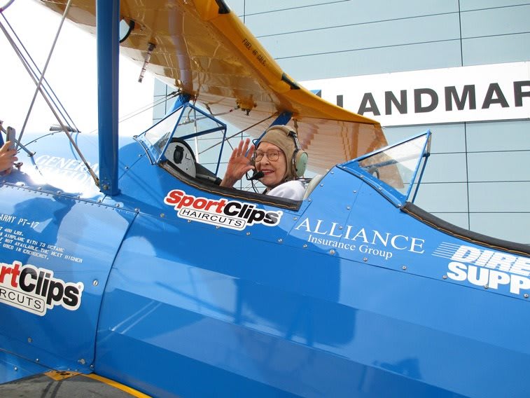A pilot waves from the cockpit of a vintage blue biplane.